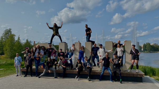 20 people posing with air guitars in front of O, U, L, U letters in a park